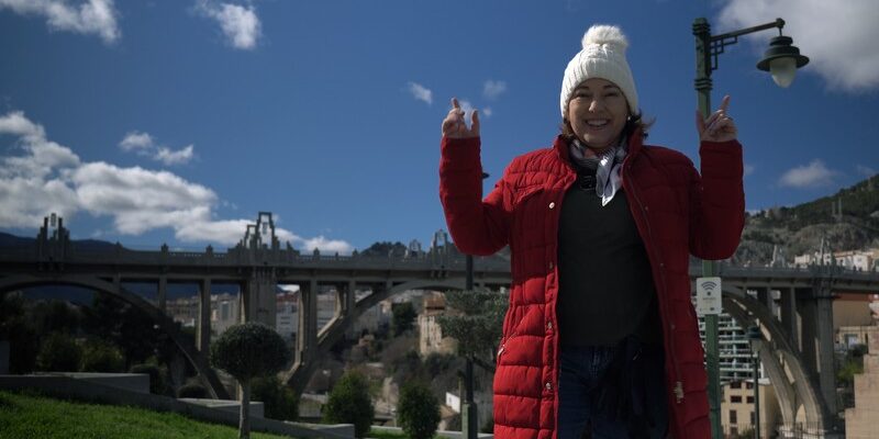 Imagen del puente de San Jordi en la ciudad de Alcoy (Alicante) en primer plano Cruz Gabaldón vestida con un abrigo rojo y un gorro blanco en un día soleado de invierno