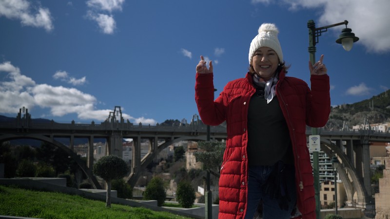 Imagen del puente de San Jordi en la ciudad de Alcoy (Alicante) en primer plano Cruz Gabaldón vestida con un abrigo rojo y un gorro blanco en un día soleado de invierno