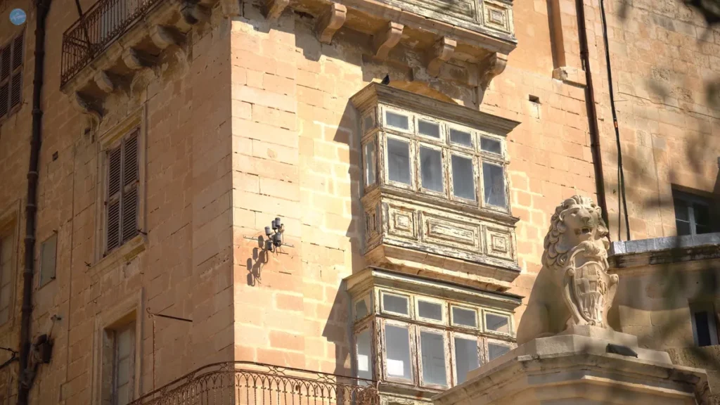 Balcón tradicional maltés de madera en un edificio de piedra caliza dorada en La Valeta, con una gárgola en forma de león en primer plano