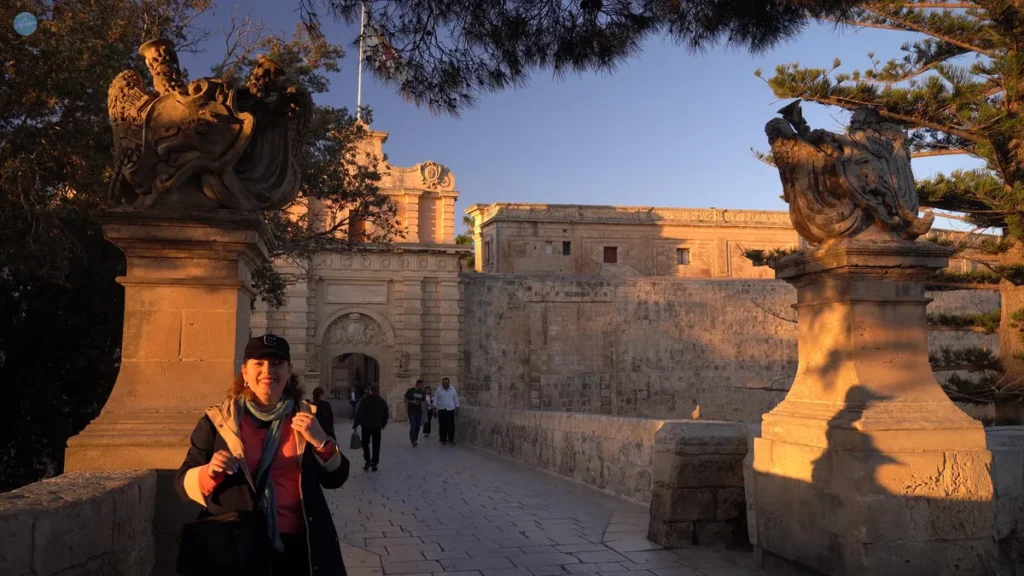 La autora frente a la Puerta Principal de Mdina al atardecer, con la luz dorada bañando las murallas de la ciudad medieval amurallada, Malta
