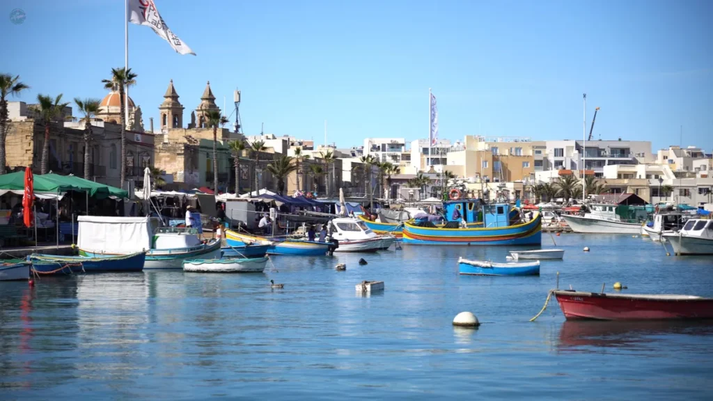 Puerto de Marsaxlokk con los luzzu, las barcas de pesca tradicionales maltesas de colores, y el mercado dominical al fondo