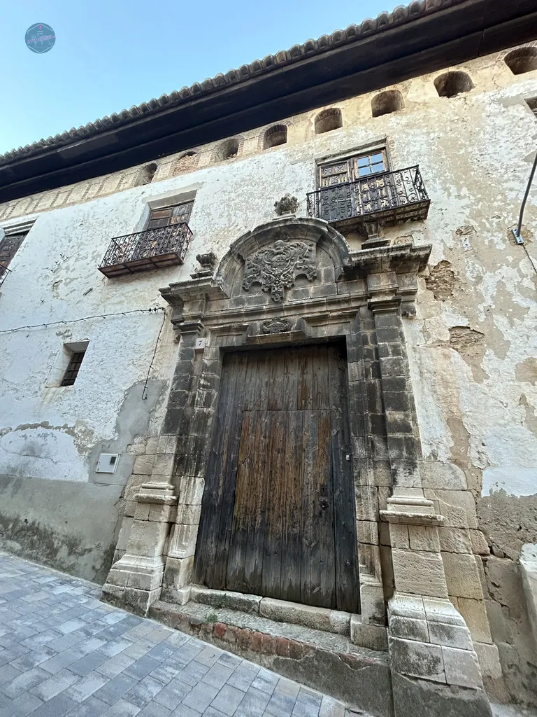 Fachada de un antiguo edificio palaciego en Benassal, mostrando portalada barroca de piedra tallada y un escudo heráldico