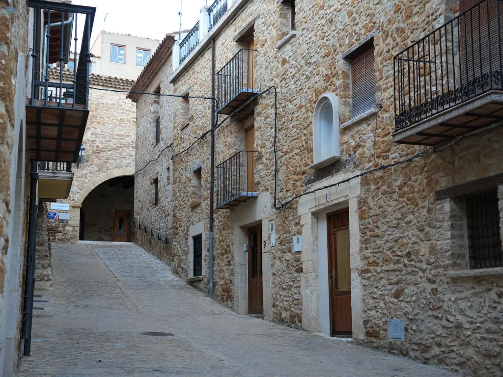 Calle empedrada del casco histórico de Benassal con fachadas de piedra tradicional y un arco medieval al fondo.