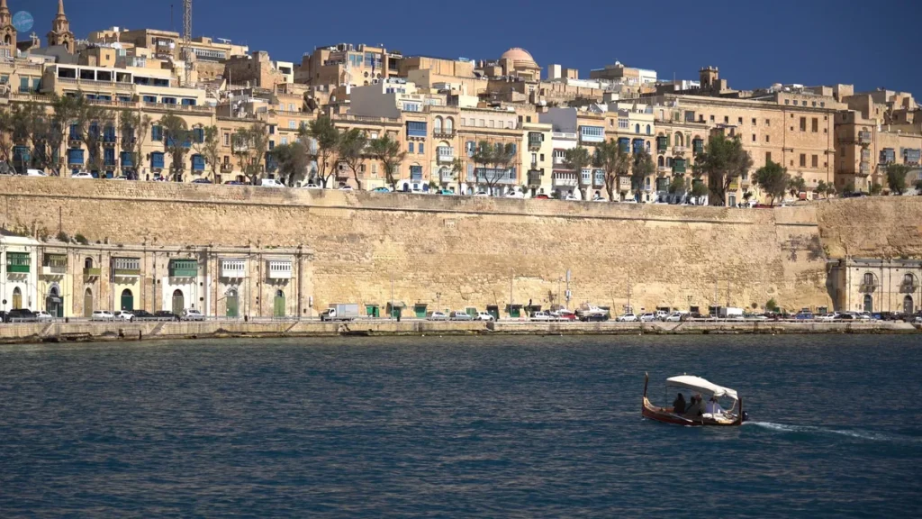 Una dgħajsa, el taxi acuático tradicional maltés, cruzando el Gran Puerto frente a las murallas y el perfil de La Valeta