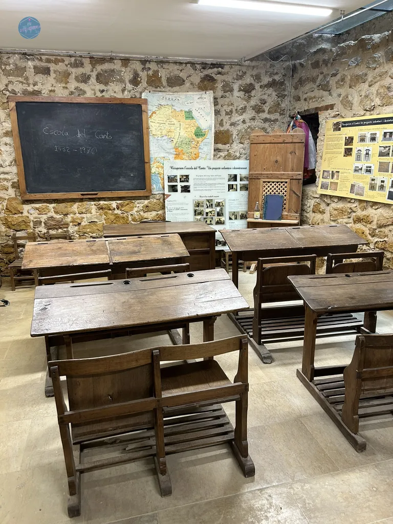 Interior de la recreación del aula histórica de la Escola del Canto (1932-1970) en Benassal, con pupitres antiguos de madera y mapas escolares.
