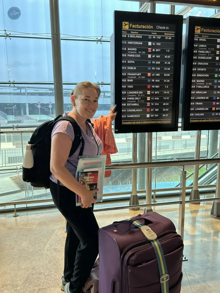 Viajera con maleta y mochila consultando el panel de facturación en un aeropuerto