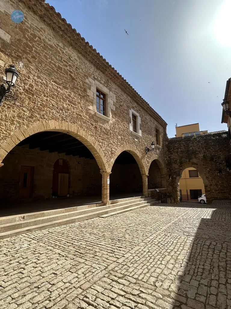 Amplia plaza porticada con suelo de adoquines y arcos de piedra en el núcleo medieval de Benassal.