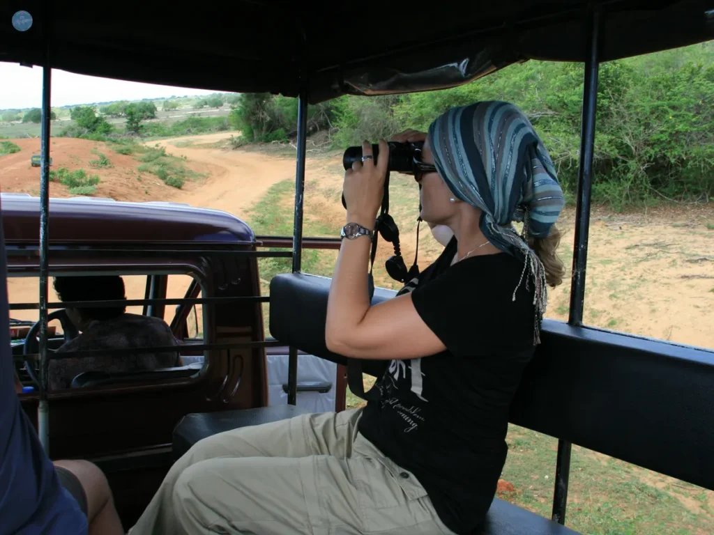 Viajera con pañuelo en la cabeza observando con prismáticos en un safari en el parque Yala, Sri Lanka