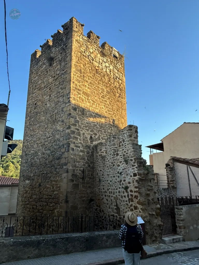 Antigua torre defensiva de piedra y restos de la muralla histórica en el casco urbano de Benassal, bajo un cielo despejado.